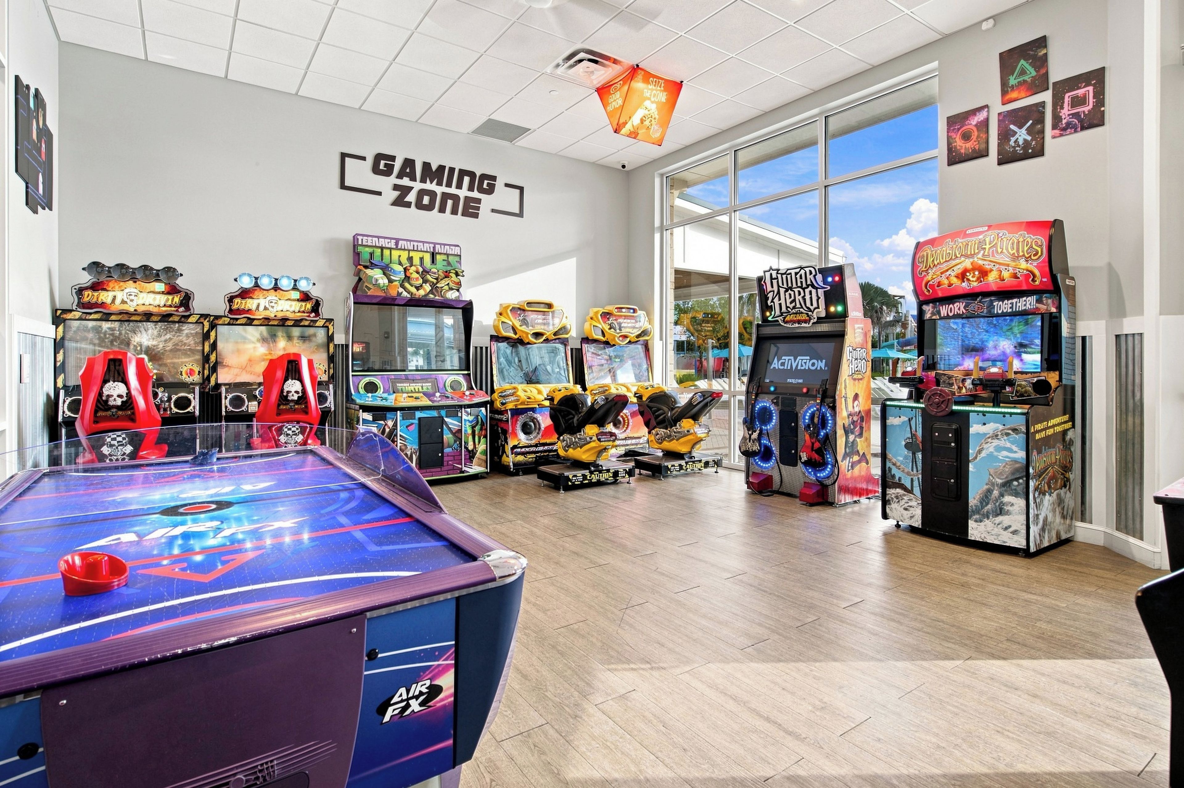 Eine Gaming-Zone mit verschiedenen Spielautomaten, einem Billardtisch und einem großen Fenster mit Blick zum Himmel.