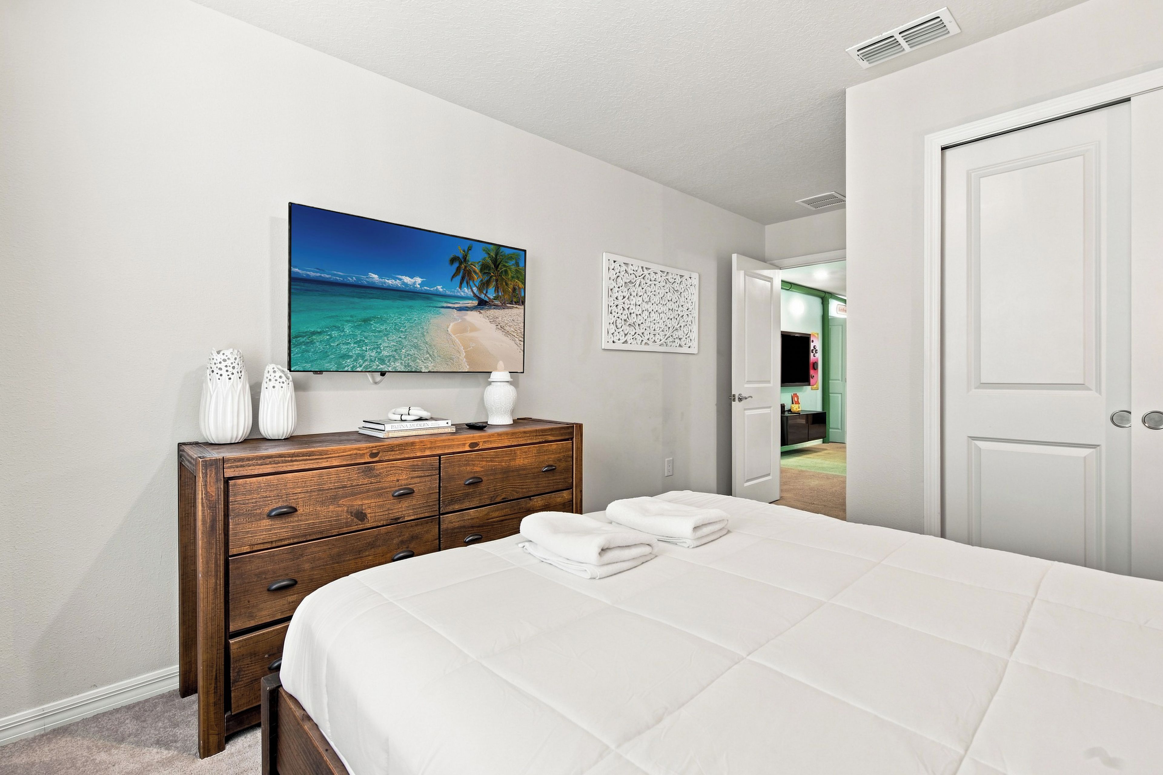 Ein Schlafzimmer mit einem Bett, einem Schminktisch, einem Strandbild und einer Tür zu einem anderen Raum.