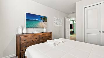 Ein Schlafzimmer mit einem Bett, einem Schminktisch, einem Strandbild und einer Tür zu einem anderen Raum.