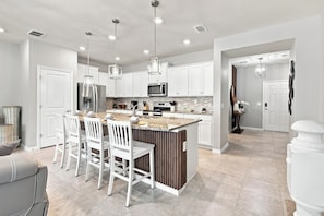 A modern kitchen with white cabinets, a central island with seating, stainless steel appliances, and pendant lighting. - Super Mario, Avengers & Harry Potter Rooms (Davenport)