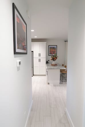 A narrow hallway leading to a kitchen with white cabinetry, a marble countertop, and a vase with flowers. - Immerse Yourself in Sedona’s Natural Beauty. (Sedona)
