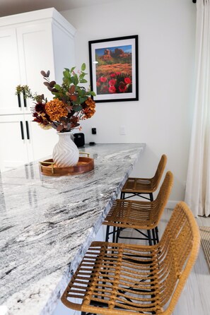 A kitchen with a marble countertop, white cabinets, a vase with flowers, and a framed picture on the wall. - Immerse Yourself in Sedona’s Natural Beauty. (Sedona)