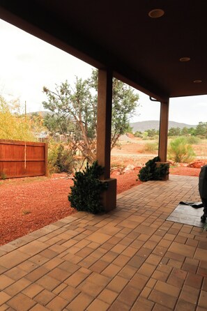 A covered patio area with a brick floor, surrounded by landscaped beds and a wooden fence. - Immerse Yourself in Sedona’s Natural Beauty. (Sedona)