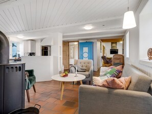 Een moderne woonkamer met een open haard, een eethoek en een keuken, zichtbaar door een open deur.