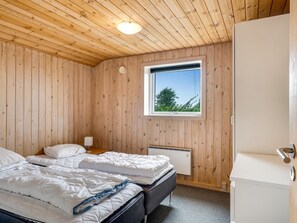 Ein Schlafzimmer mit Holzwänden, einem Fenster, zwei Betten, einem Nachttisch und einer Heizung.