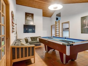 Ein Billardtisch in einem Raum mit Holzbalkendecke, einer Couch und einem an der Wand befestigten Spiegel.