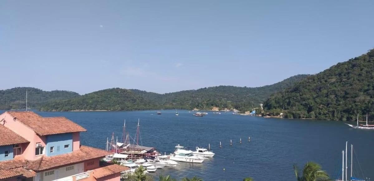 A coastal marina with boats docked, surrounded by hills and a clear sky.