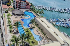 A resort with a swimming pool, palm trees, and a marina with boats.