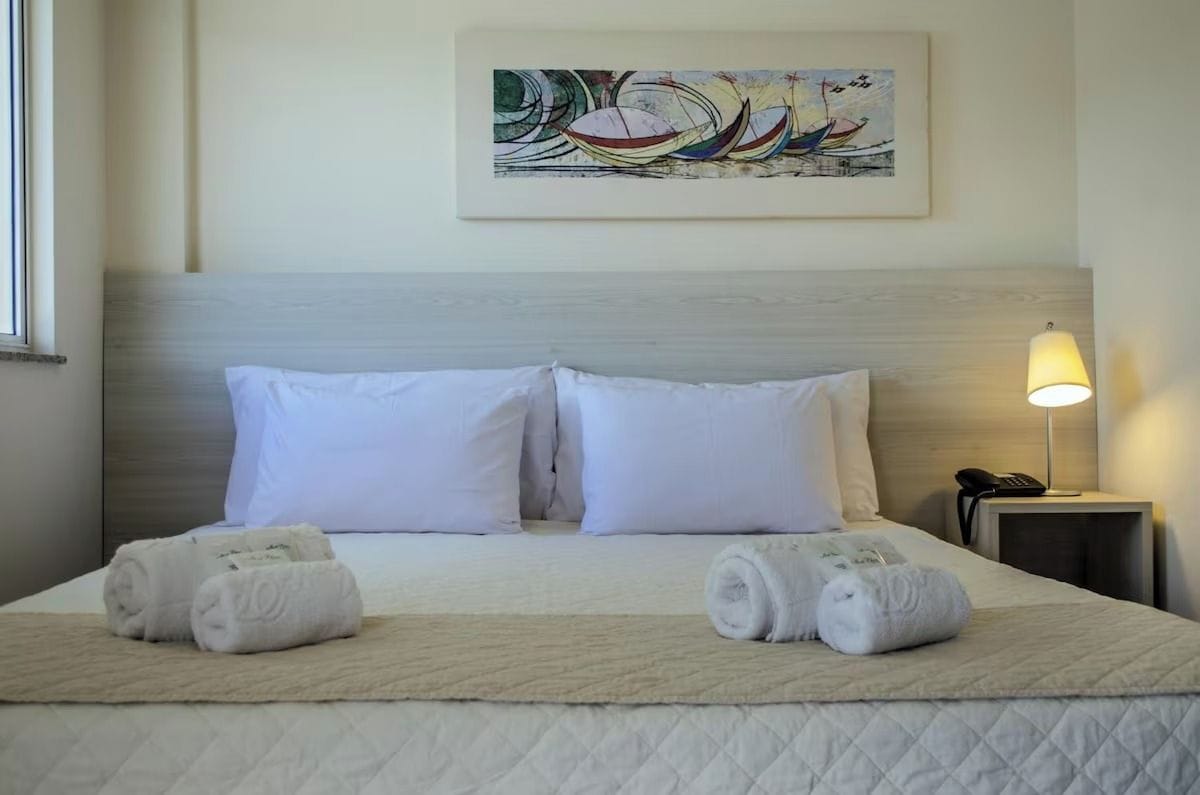 A hotel room with a bed, two pillows, a bedside lamp, a phone, and a painting on the wall.