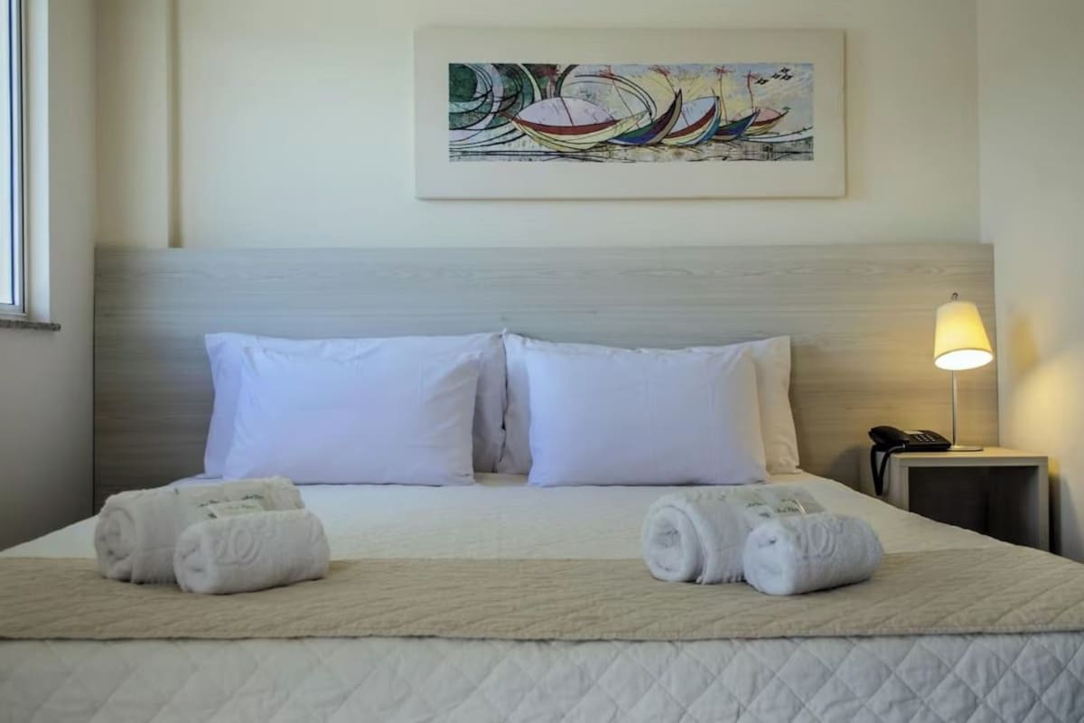 A hotel room with a bed, two pillows, a bedside lamp, a phone, and a painting on the wall.