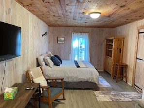 Een kamer met houten lambrisering, een bed, een televisie, een stoel, een houten kast en een raam met gordijnen.