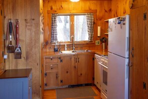 Una cocina compacta con armarios de madera, un lavamanos, un refrigerador y una ventana con cortinas a cuadros.