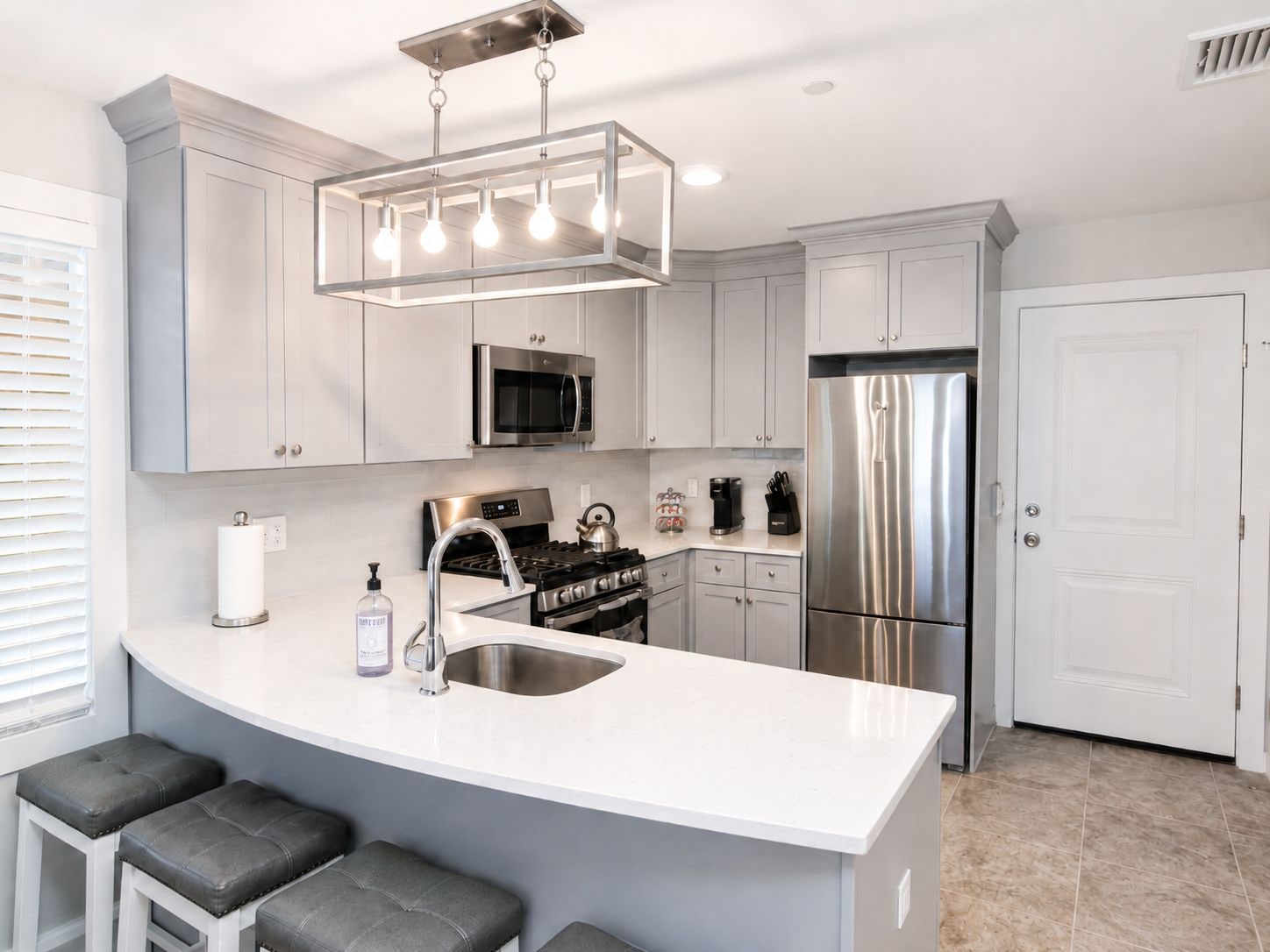 A modern kitchen with a central island, stainless steel appliances, and a hanging light fixture.