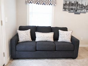 A dark grey sofa with three decorative pillows, one with 'welcome' text, and a cityscape artwork on the wall. - Stylish 3BR Retreat w/ Backyard Near MetLife, American Dream & NYC (Belleville)
