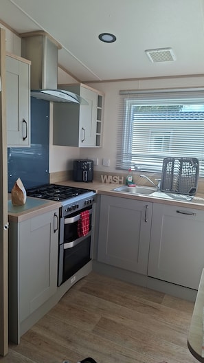 A modern kitchen with a gas stove, oven, and a built-in range hood. - 30C Kingfisher Hottub Lodge (Tattershall)