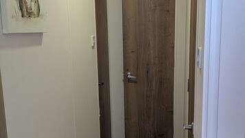 Un pasillo con puerta de madera, pared blanca con un cuadro y suelo alfombrado.