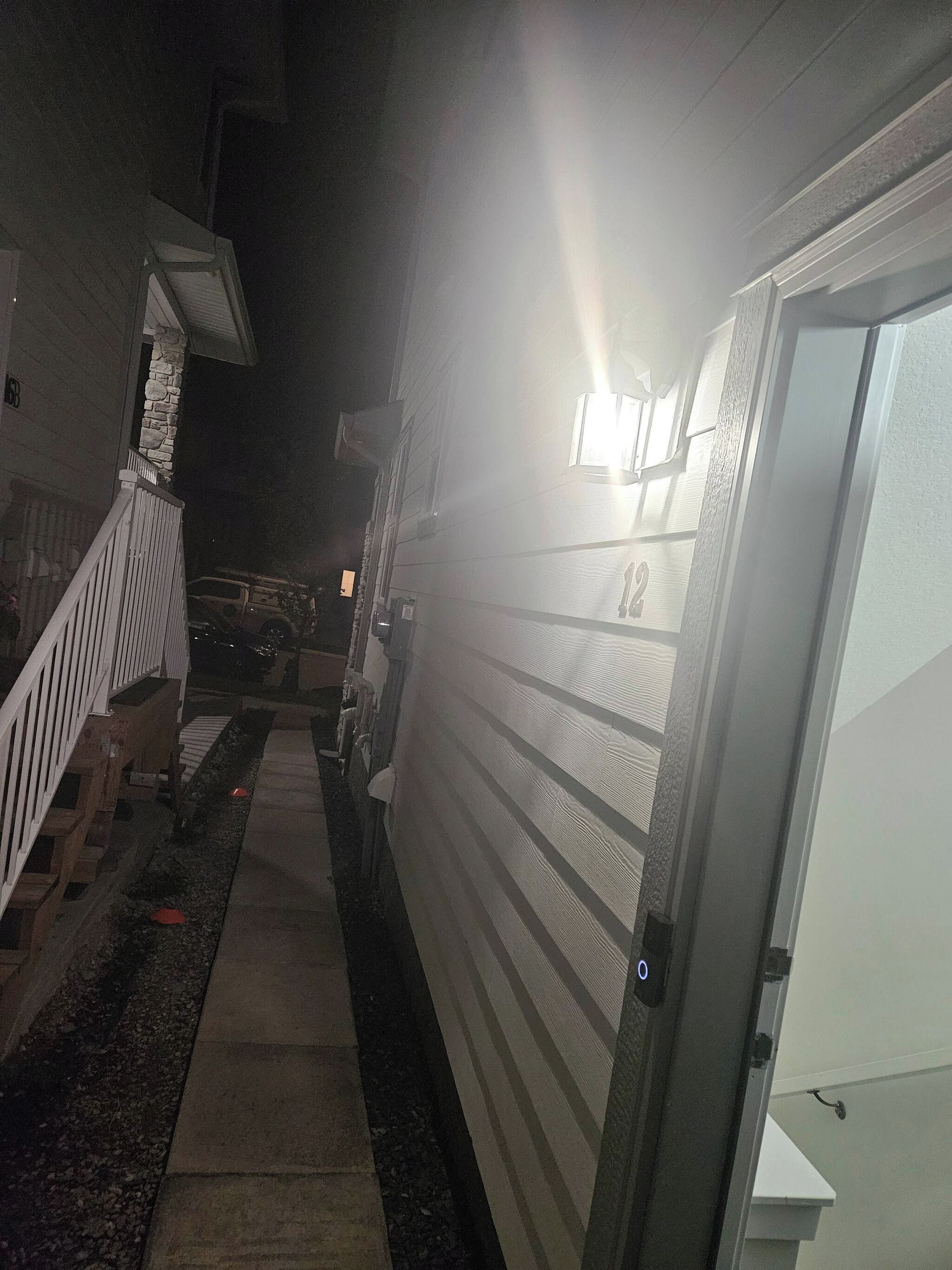 A narrow pathway leading to a building with a white door, a stone wall, and a vehicle parked outside.