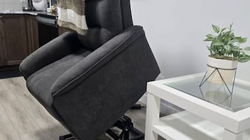 Una sala moderna con un sillón reclinable gris, una mesita auxiliar blanca con una planta y una alfombra estampada.