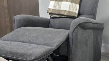 Una silla reclinable gris con reposapiés y una manta de cuadros.