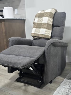 A gray reclining chair with a footrest and a checkered throw blanket.