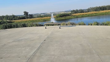 Una plataforma de hormigón con un banco y una fuente en el centro, con vistas a una masa de agua y un paisaje distante.