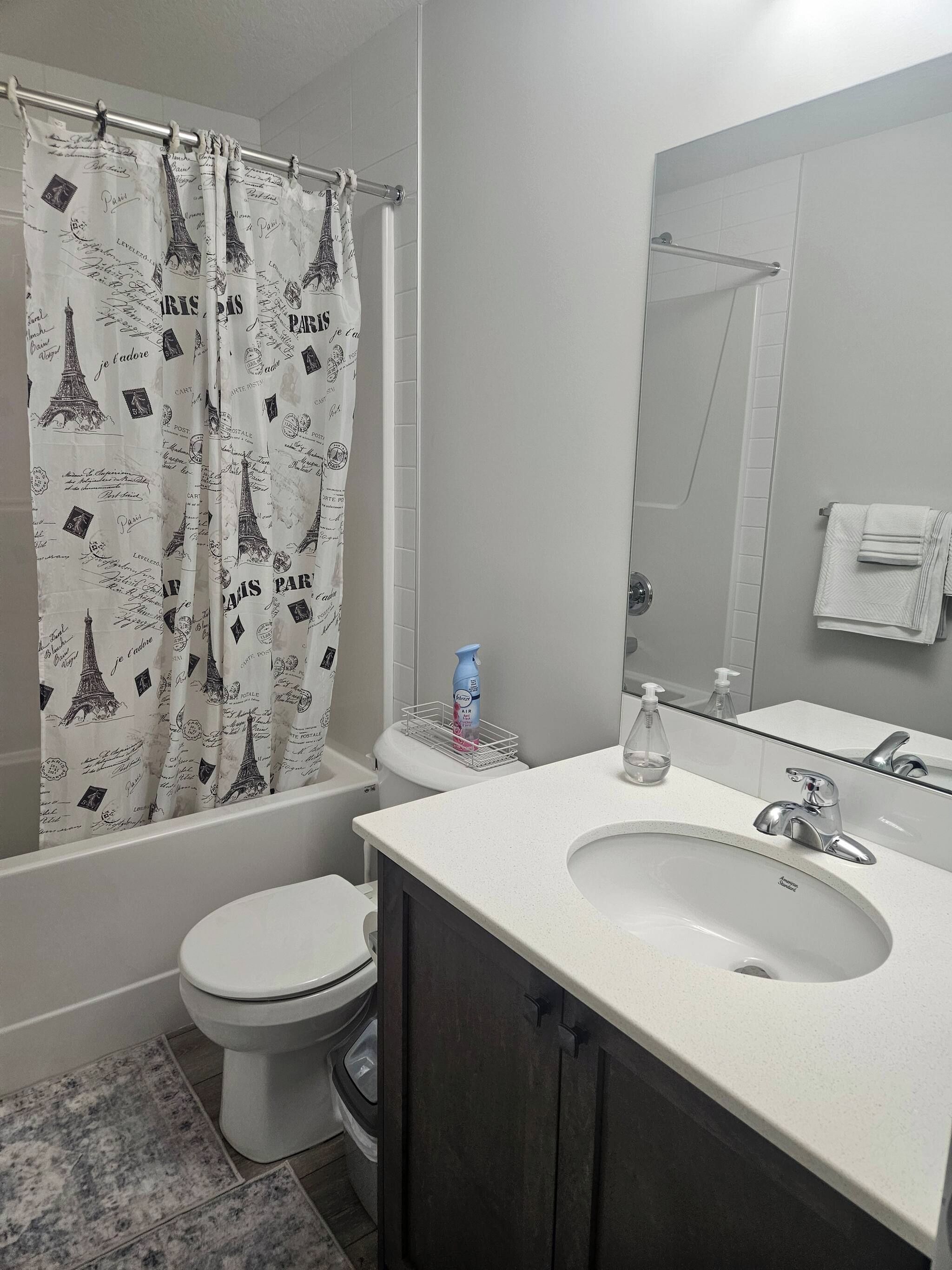 A bathroom with a shower curtain featuring the Eiffel Tower, a toilet, a sink with a mirror, and a towel rack.