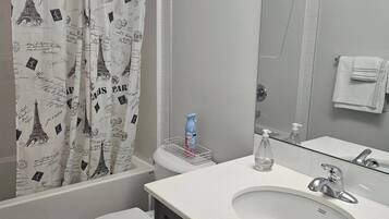 A bathroom with a shower curtain featuring the Eiffel Tower, a toilet, a sink with a mirror, and a towel rack.