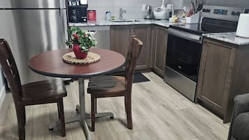 Cocina moderna con refrigerador, microondas y horno de acero inoxidable. Hay una mesa de comedor con sillas y una planta en maceta sobre la mesa.
