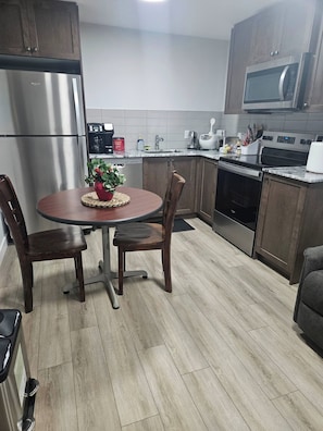 A modern kitchen with a stainless steel refrigerator, microwave, and oven. There is a dining table with chairs and a potted plant on the table. - Guest Suite in South West Calgary (Calgary)