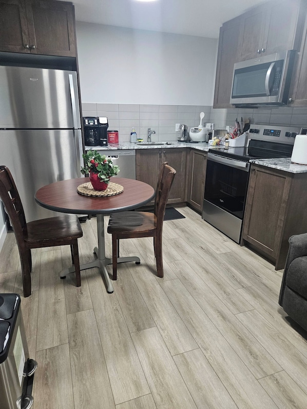 A modern kitchen with a stainless steel refrigerator, microwave, and oven. There is a dining table with chairs and a potted plant on the table.
