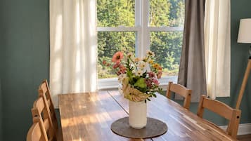 Un comedor con una mesa de madera, sillas, un jarrón con flores y una ventana con cortinas.