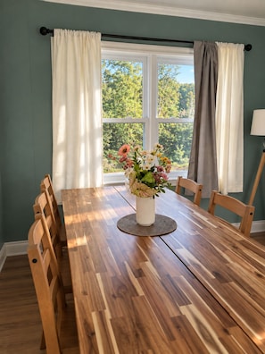 A dining room with a wooden table, chairs, a vase with flowers, and a window with curtains.