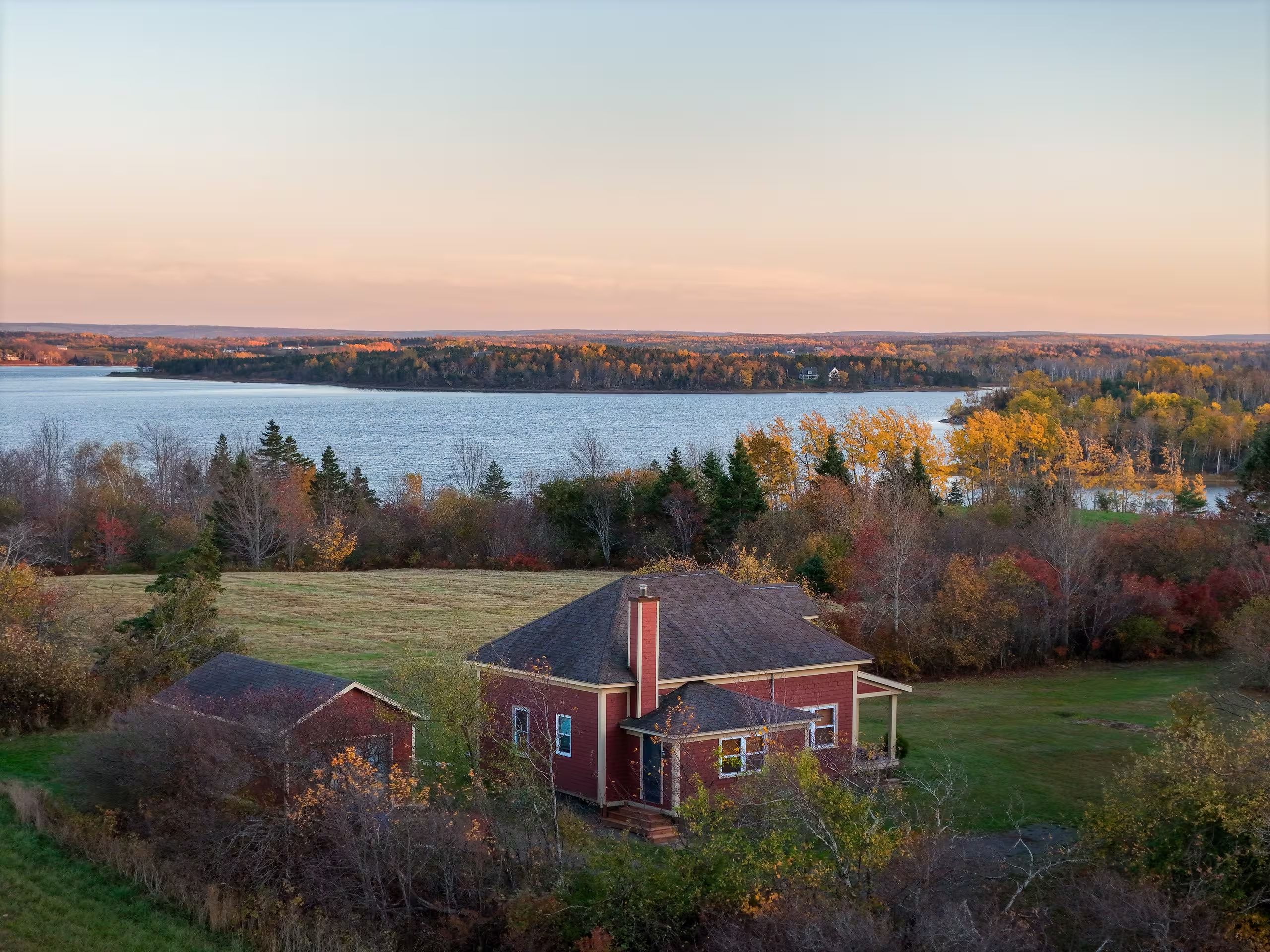 A house with a view of a lake and autumn foliage.