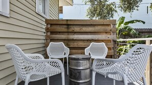 Een terras met vier witte rieten stoelen, een metalen vat en een houten omheining.