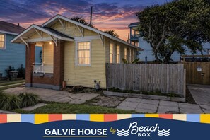 A single-story house with a front porch, a wooden fence, and a clear sky. - Galvie House | Walk to Beach + Restaurants (Galveston)