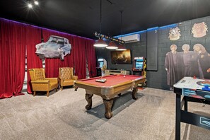 Ett rum med ett biljardbord, en röd gardin, en upphängd bil och en vägg prydd med en Harry Potter-affisch.
