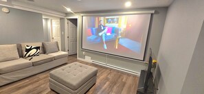 Un salon avec un grand écran, un canapé, un pouf et une porte.