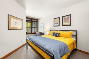 Ein Schlafzimmer mit einem Bett, einem Nachttisch, einem Fenster und gerahmten Bildern an der Wand.