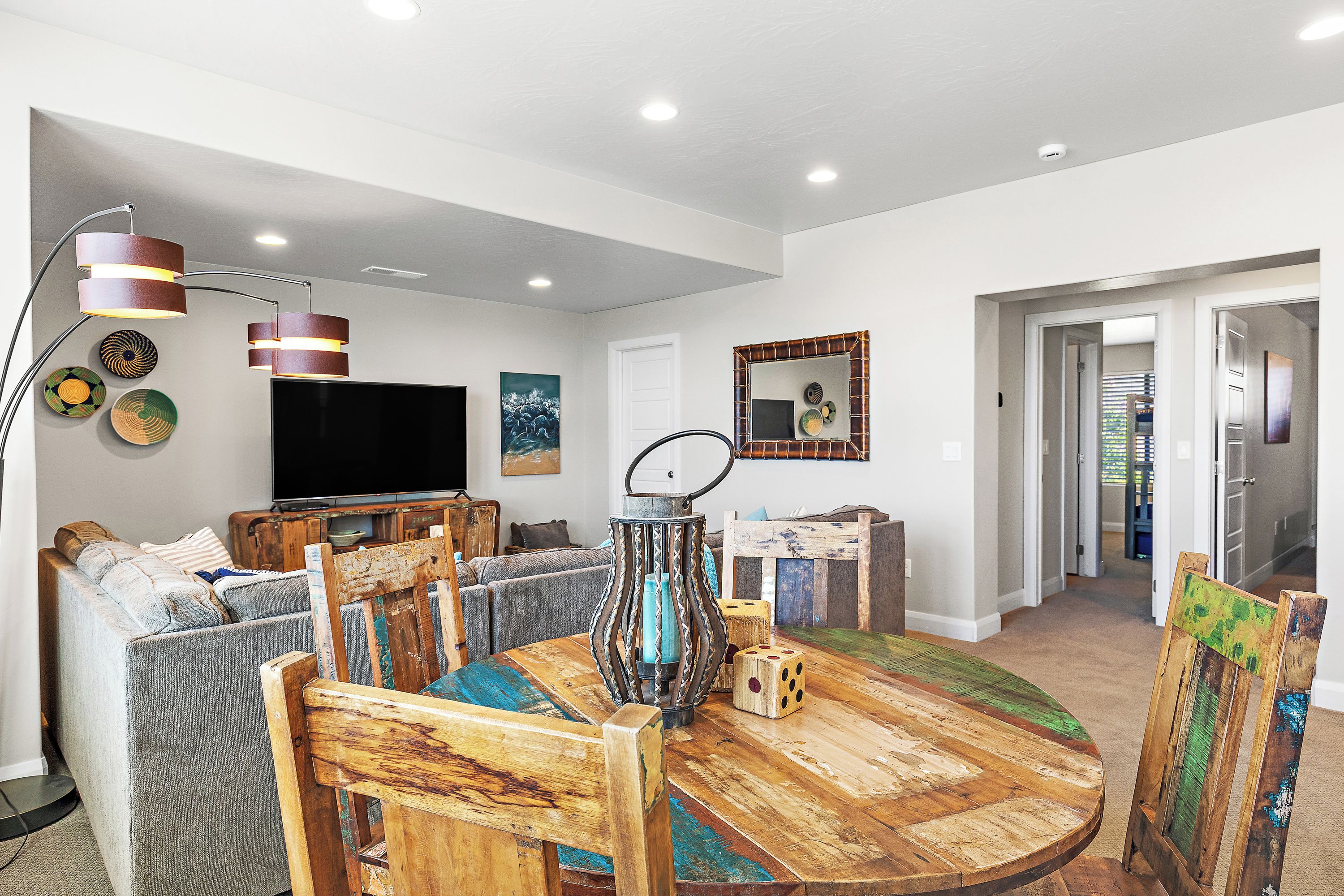 A modern living room with a round wooden dining table, a sofa, a television, and a decorative mirror.