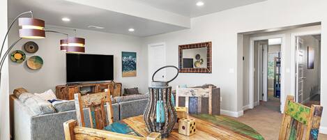 A modern living room with a round wooden dining table, a sofa, a television, and a decorative mirror.