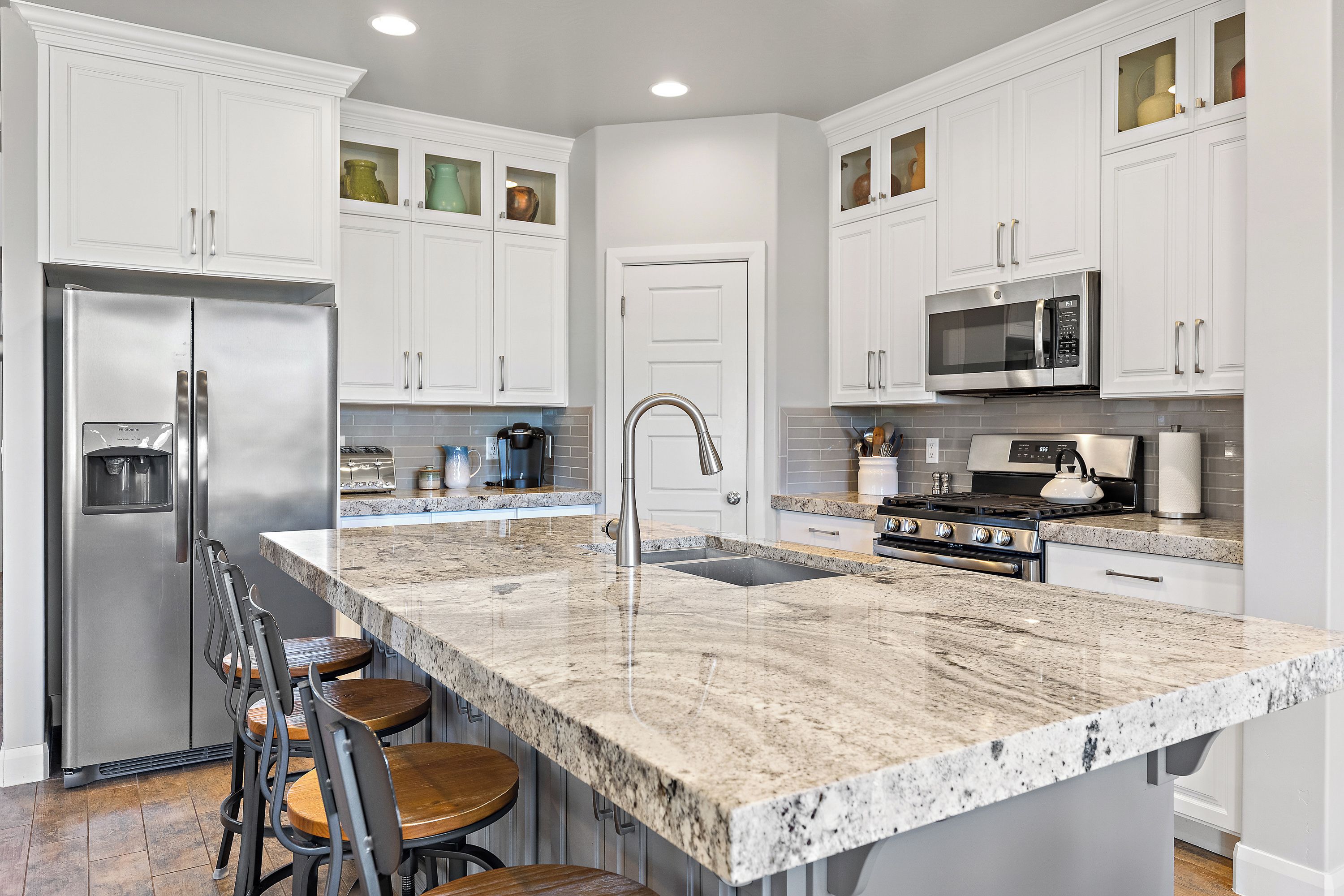 A modern kitchen with white cabinetry, stainless steel appliances, a granite countertop, and a bar area with stools.