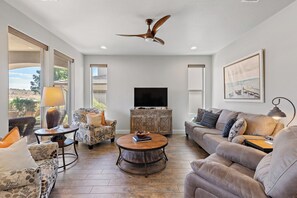 A living room with a large window, a ceiling fan, a television, and a painting on the wall. - 4BR, 4BA villa in Sienna Hills with pool, hot tub & resort amenities. (Washington)