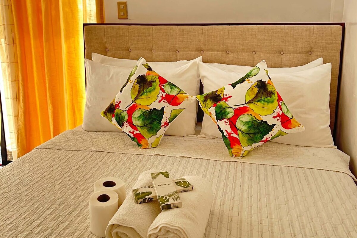 Una cama bien tendida con dos almohadas decorativas, un juego de toallas y un letrero en la pared.