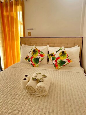 Una cama bien tendida con dos almohadas decorativas, un juego de toallas y un letrero en la pared.