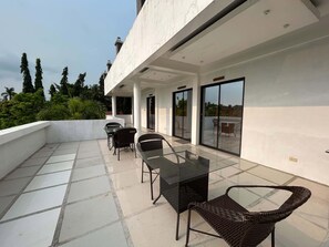 Un patio moderno al aire libre con una mesa y sillas de vidrio, vistas a la vegetación circundante y un cielo despejado.