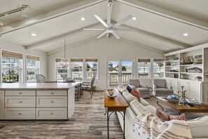 A spacious living area with a high ceiling, a large island with a kitchen counter, and a seating area with a sofa and chairs.