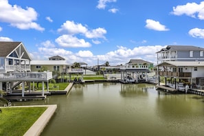 A waterfront property with a dock, a covered boat launch, and a grassy area. - Casa Flamingo- Canal Front | Great for Families (Galveston)