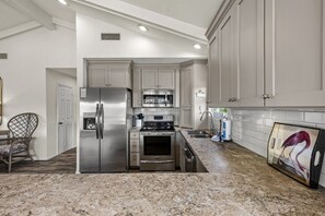 A modern kitchen with stainless steel appliances, white cabinetry, and a granite countertop.