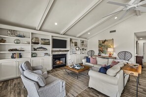 Una sala de estar con chimenea, muebles blancos y objetos decorativos en estanterías.