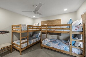 Habitación con literas, un ventilador de techo, un pequeño banco y una tabla de surf en la pared.